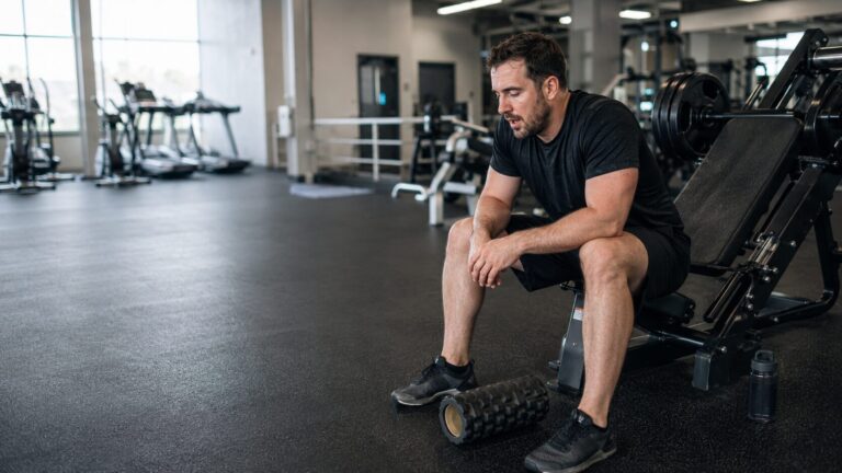 Tired man sitting beside a leg press after doing. too much during his warm-up